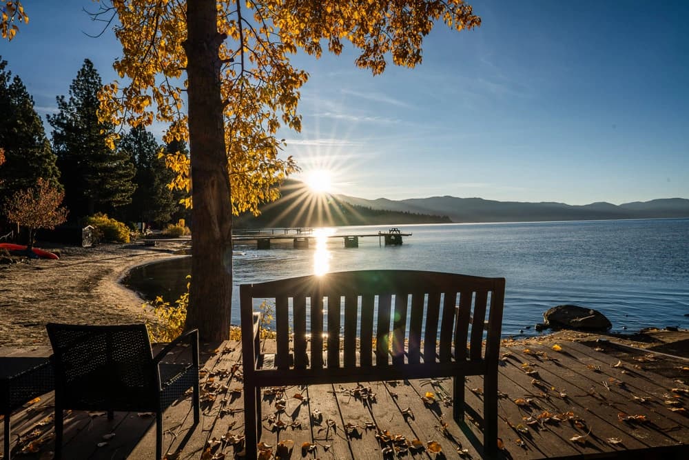 Bench on lakeside deck at sunrise with golden leaves and pier reflecting on Lake Tahoe