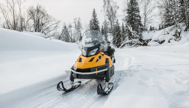 Bright yellow snowmobile parked on a snowy mountain trail surrounded by pine trees in Tahoe Vista, CA.